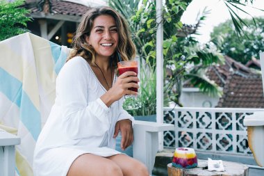 Keyifli, neşeli, neşeli bir kadın kahvaltıda kırmızı içecek ve meyveli tatlıyla dışarıda keyif çatıyor.