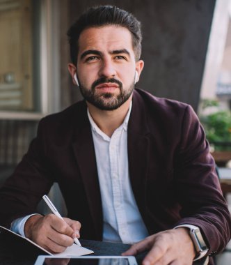 Düşünceli İspanyol işadamı, balkonda kablosuz kulaklıkla müzik dinlerken ve not defterine yazarken başka tarafa bakıyor ve düşünüyor.