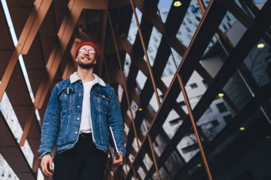 Tablet taşıyan ve şehir merkezinde modern cam gökdelenlerle gezen modaya uygun giyinmiş neşeli bir adamdan.