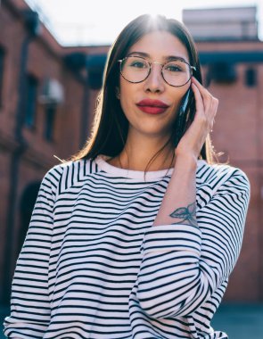 Gözlüklü çekici bir kızın yarı boy portresi. Şehir sokağındaki boş zamanlarında kameraya bakıyor. 4 g 'lik interneti telefonla kullanan güzel bir kadın.