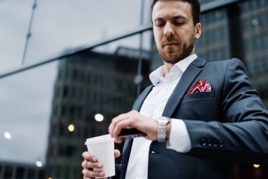 Modern şehir merkezinde kahve molası verirken şık takım elbiseli ciddi bir erkek yöneticinin kol saatini kontrol etmesinden.