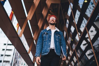 Tablet taşıyan ve şehir merkezinde modern cam gökdelenlerle gezen modaya uygun giyinmiş neşeli bir adamdan.