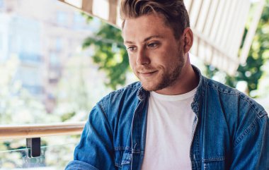 Gündelik giyinen zeki genç erkek öğrenci dışarıda, kafenin terasında dizüstü bilgisayarla çalışırken yazı yazma notları alıyor.