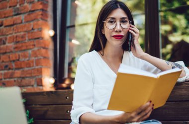 Kafe terasında modern netbook ile oturan serbest kadın portresi cep telefonu uygulaması üzerinden arama yapan, zaman yönetimi için not defteri tutan Latin kadın.