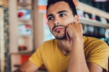 Modern kafede boş ekran dizüstü bilgisayarla otururken eline yaslanıp kompozisyon yazan düşünceli, genç bir erkek öğrenci.