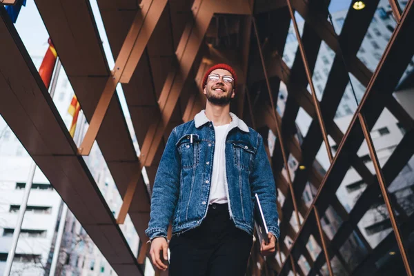 Tablet taşıyan ve şehir merkezinde modern cam gökdelenlerle gezen modaya uygun giyinmiş neşeli bir adamdan.