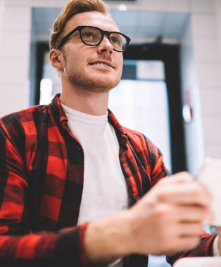 Kareli tişörtlü, neşeli, dikkati dağılmış, cep telefonuna göz gezdiren, iş yerindeki serbest çalışma projesinde çalışan ve gözlerini başka yöne çeviren bir adamdan.