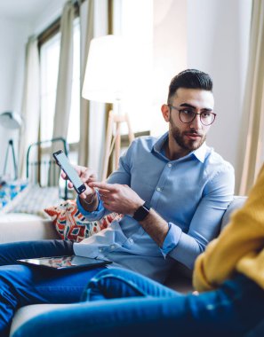 Çift evdeki kanepede oturup sohbet ederken ve birbirlerine bakarken cep telefonlarını paylaşıyor.