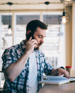 Kendine güveni tam ciddi bir adam iş arkadaşıyla konuşuyor telefon paylaşımı hakkında kitap okuyor kahve dükkanında masada oturuyor.