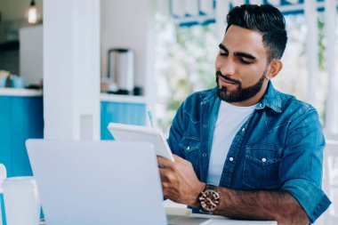 Modern açık hava kafedeki laptopta araştırma için notlar alırken şık giyinmiş, güler yüzlü etnik erkek öğrenci.