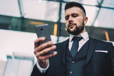 Modern şehrin merkezindeki çağdaş bir binanın önünde dikilirken, takım elbiseli, kaşlarını çatan ve akıllı telefonlara bakan iş adamlarından.