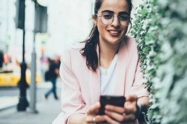 Modern şehrin kentsel sokaklarında kameralara bakarak arkadaşlarıyla akıllı telefon mesajları kullanan gündelik kıyafetleri ve gözlükleriyle hoş bir bayan.