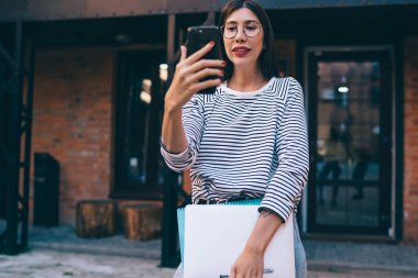 Çekici genç bir kadın cep telefonuyla görüntülü arama yapıyor. Şehir merkezinde duruyor ve halka açık internet bağlantısını telefon etmek için kullanıyor. Güzel kadın blogcu not yayınlıyor.