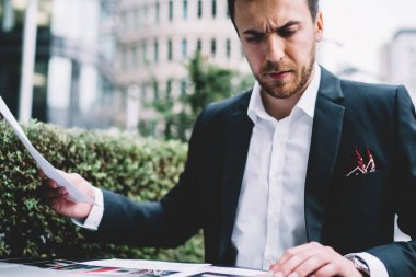 Şehir terasında dizüstü bilgisayarla uğraşırken resmi takım elbiseli, şirket belgelerini dikkatle inceleyen yoğun bir çalışan.
