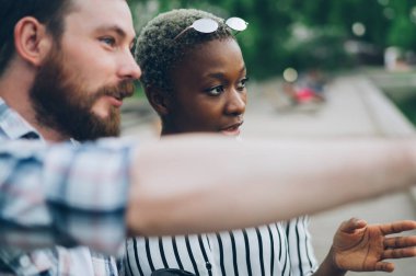 Sakallı adam parkın bulanık arka planına gitmek için içkili Afrikalı Amerikalı bayana güzergahı gösteriyor ve anlatıyor.