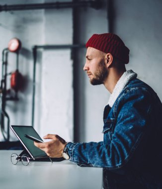 Genç dalgın sakallı, stil sahibi serbest stil sahibi, sıcak mavi kot ceket giyen, kırmızı şapkalı iş yerindeki aletleri kullanan