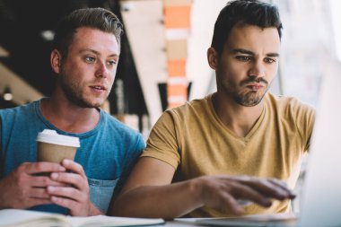 Laptop kullanan ve kahve içerken ve kafede otururken başlangıç projesi üzerinde çalışan konsantre erkek serbest çalışanlar.