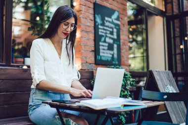 Optik gözlüklü milenyum öğrencisi üniversite dersleri için dijital bilgi araştırması yapıyor. İnternet sitelerini taramak için internet bağlantısı olan sokak kafeteryasında oturuyor.