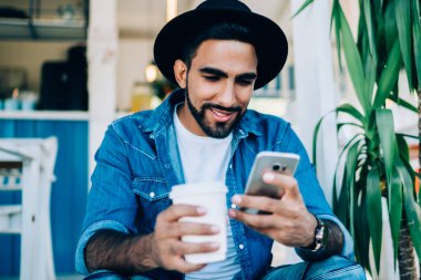 Kot pantolon ve şapka takan konsantre İspanyol erkek şehir kafesinin merdiveninde kahve içerken rahatlıyor.