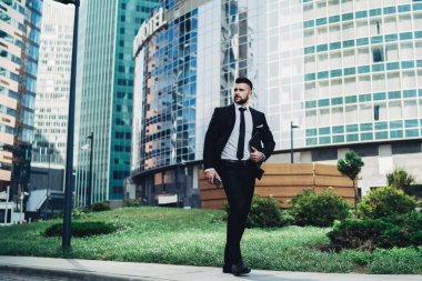 Siyah takım elbiseli, kendinden emin genç bir erkek. Gezici ve not defteri ile güneşli bir günde eşiyle buluşmaya gidiyor.