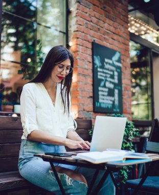 Optik gözlüklü milenyum öğrencisi üniversite dersleri için dijital bilgi araştırması yapıyor. İnternet sitelerini taramak için internet bağlantısı olan sokak kafeteryasında oturuyor.