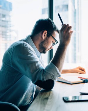Mavi gömlekli, gözlüklü, aklı başında bir entelektüel. Pencere karşısında dizüstü bilgisayarla masada oturan not defterini kontrol ediyor.