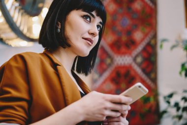 Havalı kıyafetli modaya uygun bir bayan, rahat bir doğu kafesinde akıllı telefonlara bakarken başka yöne bakıyor ve düşünüyor.