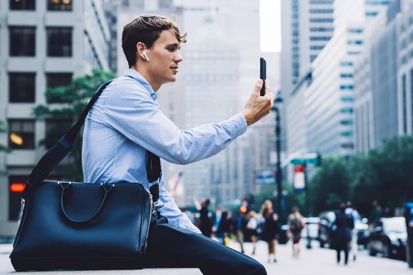 Side view of executive male person communicating with service operator for online consultancy about 4g roaming internet for business trip, young proud ceo in earbuds using bluetooth for calling