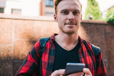 Kırmızı-siyah tişörtlü ve siyah tişörtlü mutlu bir erkek yazın şehirde gezintiye çıkıyor.