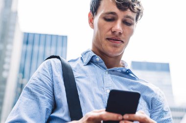 New York 'un ortasında deri çantalı çekici, çağdaş bir adam telefonla mesaj atıyor. Kendinden emin görünüyor.