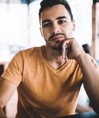 İyimser, yakışıklı, bıyıklı genç bir erkek. Eline yaslanmış, kafeteryada kameraya bakarak vakit geçiriyor.