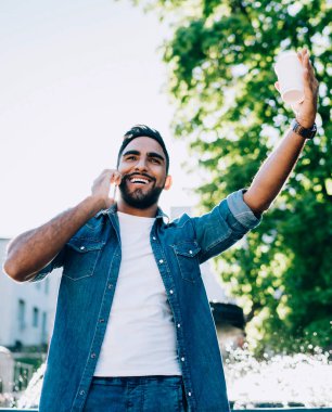 Kot elbiseli, şık İspanyol bir adamdan yükseltilmiş bir içecekle sokakta dikilip bulanık manzaralı bir yaz parkına karşı telefonla konuşurken arkadaşına gülümsüyor ve onu selamlıyor.