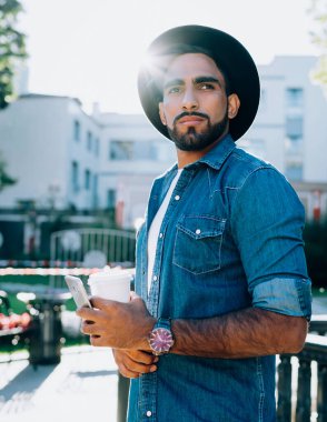 Şapkalı ve kot ceketli İspanyol serbest aksanlı, gözlerden uzak duran ve sokakta dikilirken karar veren ucuz bir modacı.