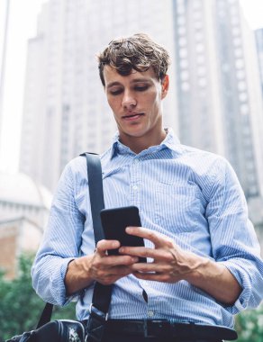 Deri çantalı genç işadamı New York 'un yüksek binalarının arkasında telefonla mesajlaşıyor.