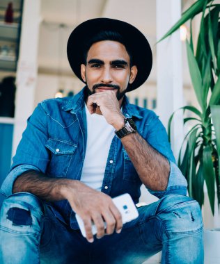 İspanyol asıllı, kendine güveni tam, modaya uygun kot giyen, cep telefonuyla takılan ve kafenin merdivenlerine yaslanmış kameraya bakan bir adamdan.