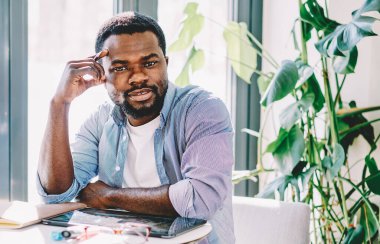 Uzaktan çekim sırasında tabletle masada oturup kameraya bakarken kendine güveni tam, sakin bir serbest çalışan.