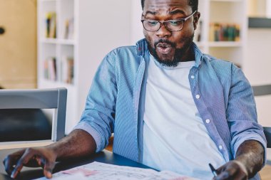 Neşeli Afro-Amerikalı adam modern ofisteki masanın planlarını incelerken heyecandan homurdanıyordu.