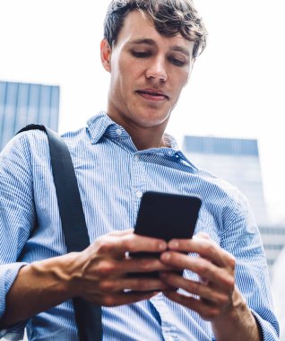 New York 'un ortasında deri çantalı çekici, çağdaş bir adam telefonla mesaj atıyor. Kendinden emin görünüyor.