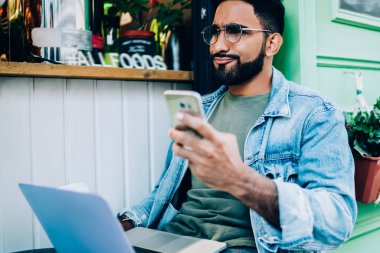 Hüsrana uğramış modern adam elinde cep telefonu tutan ve haberlerden memnun kalmayan kafenin yanındaki bankta dizüstü bilgisayarla oturan