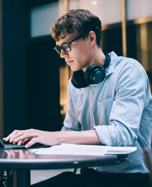 在纽约市曼哈顿 年轻英俊 专心致志 戴着耳机 戴着眼镜的男人坐在工作场所的桌子旁 — 图库照片