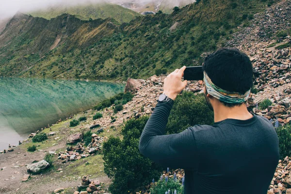 Male in active wear using smartphone technology with image application for creating wonderful multimedia content of water reflection of high mountains, man clicking pictures during trekking adventure