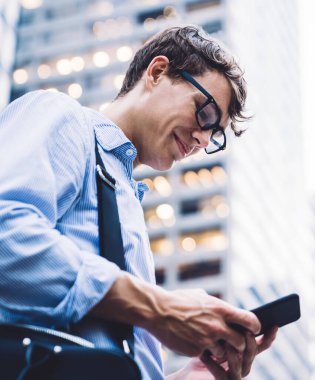 New York 'un arka planında duran, çantalı, çantalı, cep telefonlu, tişörtlü ve gözlüklü işçilerin yan görüntüsü.