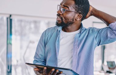 Kafası karışan, günlük kıyafetli, tabletli, kafası kaşınan, problem üzerinde kafa yoran, modern ofis projesinde çalışan kafası karışık bir zenci.