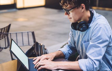 Gözlüklü, gözlüklü, tabletini karıştıran yakışıklı genç adam Manhattan, New York 'ta iş yerinde belgelerle masada oturuyor.