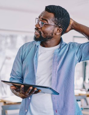 Kafası karışan, günlük kıyafetli, tabletli, kafası kaşınan, problem üzerinde kafa yoran, modern ofis projesinde çalışan kafası karışık bir zenci.