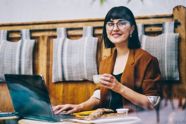 İçerik tarzı gözlüklü, siyah saçlı, sıradan bir ceket giyen, etnik kafede kahve molası verip gözlerini kaçıran bir kadın.