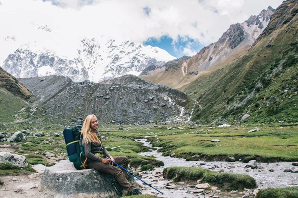 Portrait of cheerful carefree hiker smiling at camera during recreation trekking tour around breathtaking mountains with scenic views, happy woman with touristic rucksack enjoying travel adventure
