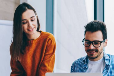 Ofiste dizüstü bilgisayar işbirliği ile çalışma yerine yakın pozitif gülümseyen erkek ve kadın, araştırma için kablosuz kullanarak samimi bir ortamda startup paylaşmak fikirleri üzerinde işbirliği erkek ve kadın çalışanlar