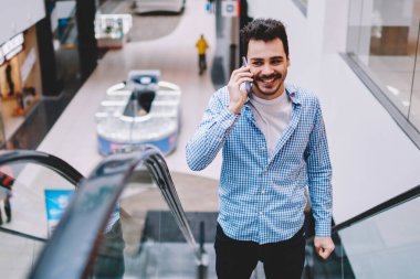 Neşeli adam şık rahat giyim giyinmiş dükkanlar boş zamanlarında arkadaşa çağrı ile tanıtım alanında ikinci kata üst katta tırmanan, mutlu adam akıllı telefon konuşma sırasında gülüyor