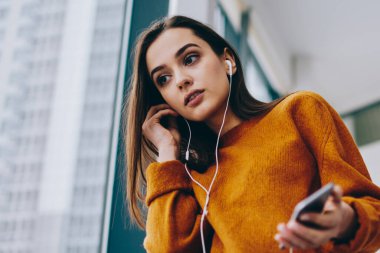 Akıllı telefon uygulaması üzerinden radyo online dinlemek için kablosuz 4g bağlantısı kullanarak rahat bir görünüm giymiş kafkas hipster kız pondering, şarkı zevk elektronik kulaklık düşünceli kadın